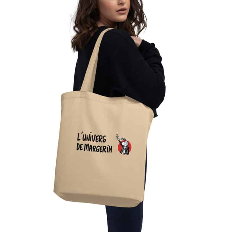 Tote bag beige "L'Univers de Margerin" porté à l'épaule, avec logo inspiré de l'univers de Frank Margerin.